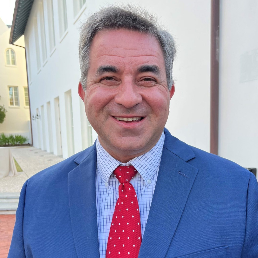 A headshot of a man dressed in a blue suit jacket and a red tie.